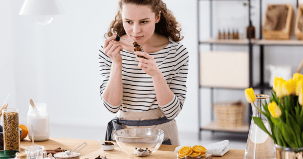 woman smelling essential oil while preparing natural homemade hair detangler spry in a kitchen